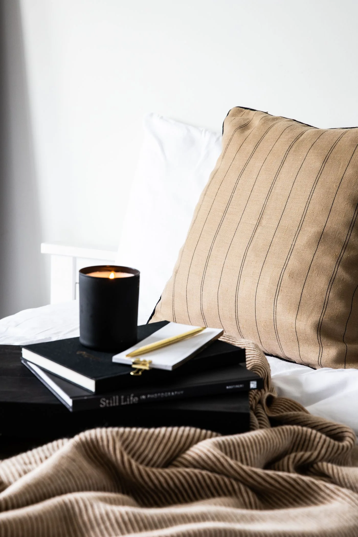 A candle and a small stack of books on soft bedding