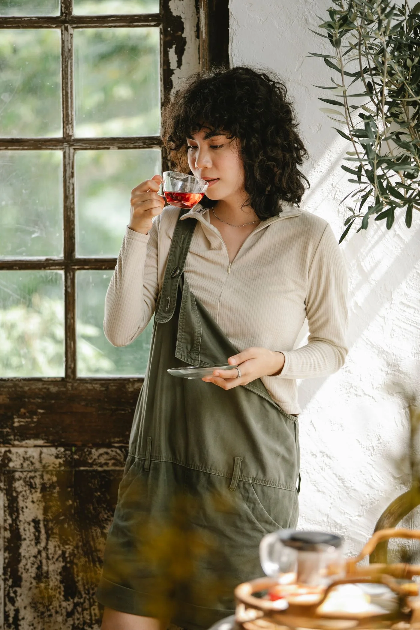A woman pausing with a glass of tea beside a rustic window