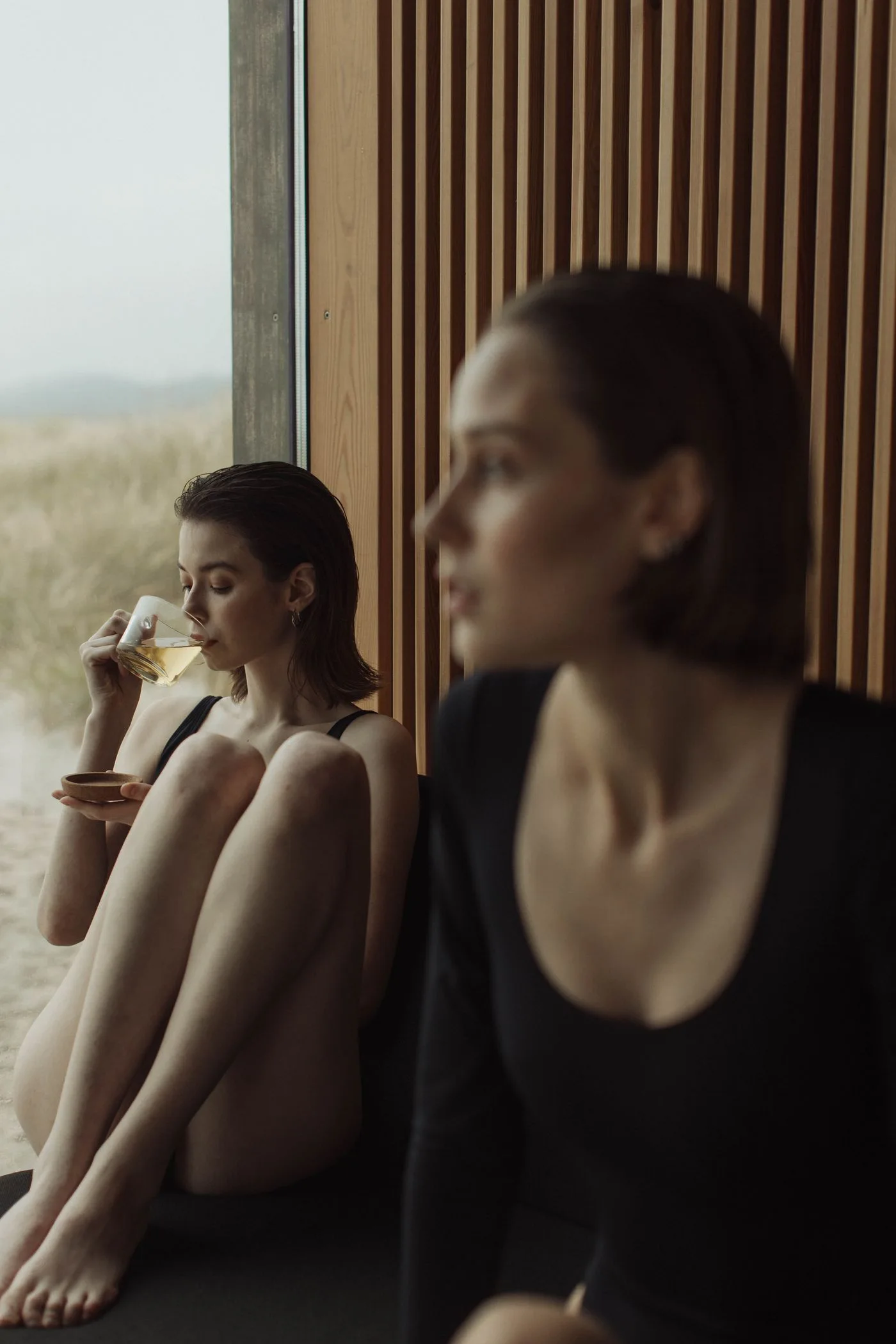 Two women quietly sipping tea beside a large window