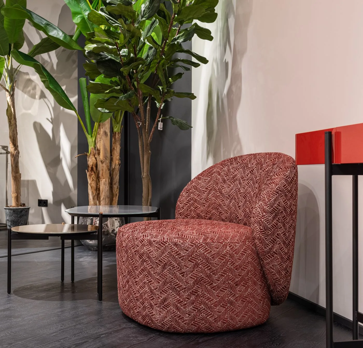A red armchair beside green plants and a small side table