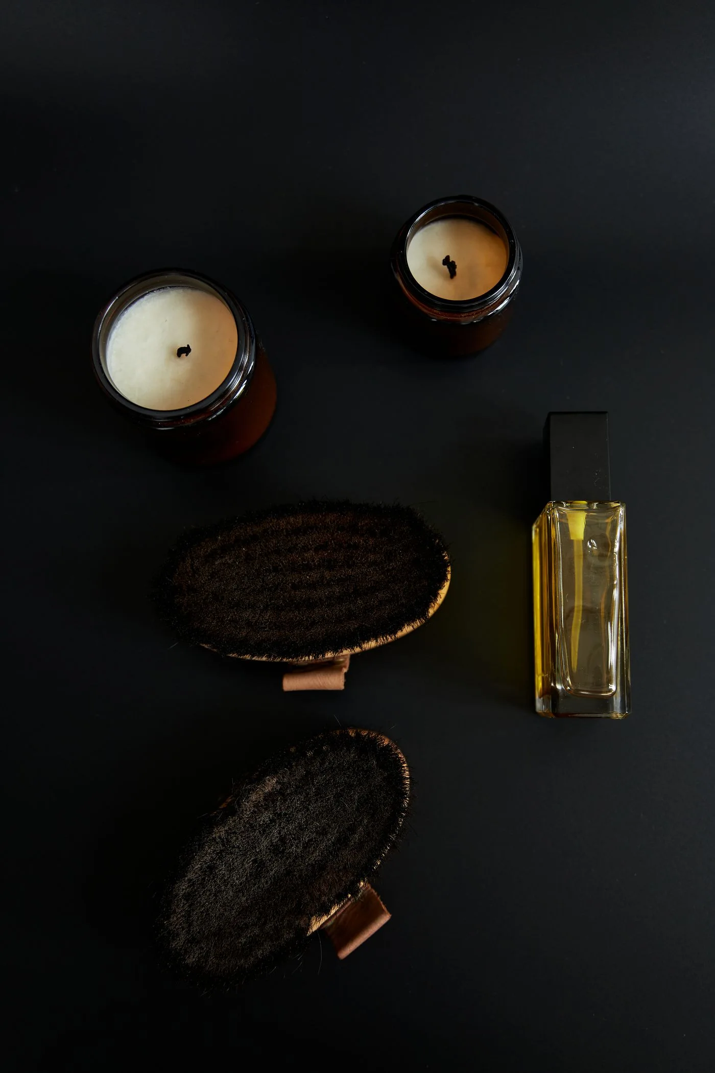 A body brush, candle and bath oil arranged on a dark surface